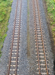 Symmetrical aerial view of dual railway tracks over gravel and surrounded by grassy terrain.