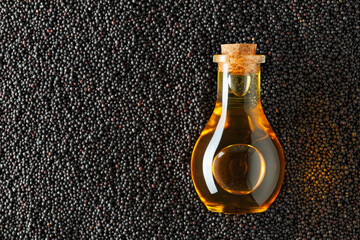 Glass bottle containing golden oil resting on bed of rape seeds, highlighting the rich color contrast and the natural origin