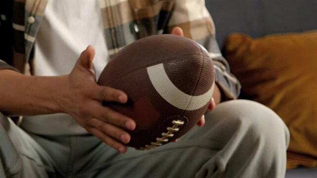 Close-up of tensed African American male supporter with football ball watching American football match on tv, emotionally supporting favorite team at home.