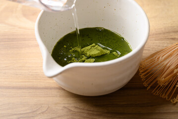 Matcha green tea powder mixing with water in tea bowl
