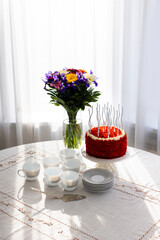 Bithday cake called Red Velvet with twisted silver candles on laid table with porcelain cups, saucers and colorful flower bouquet
