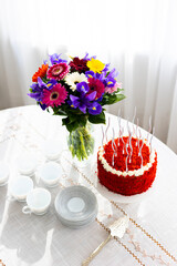 Bithday cake called Red Velvet with twisted silver candles on laid table with porcelain cups, saucers and colorful flower bouquet
