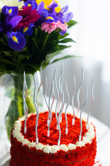 Bithday cake called Red Velvet with twisted silver candles on laid table with porcelain cups, saucers and colorful flower bouquet
