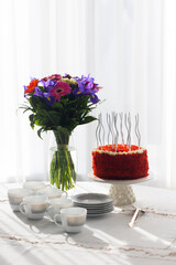 Bithday cake called Red Velvet with twisted silver candles on laid table with porcelain cups, saucers and colorful flower bouquet

