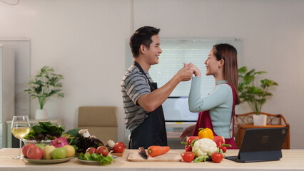 Happy couple holding hands and dancing in kitchen while preparing ingredients for a healthy meal