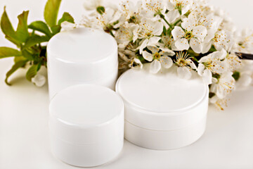 Mockup. Cosmetic cream jars placed near delicate white flowers and green leaves. Cream represents natural skincare freshness. Concept beauty cream for organic cosmetic branding and skincare promotions