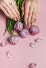 Woman hands with perfect nude manicure holding pink tulips on pink background
