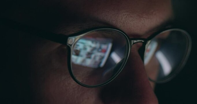 Close up portrait of male in glasses with reflection of computer screen working online. Close up male eyes in eyeglasses working late at night scrolling internet pages in front of laptop computer