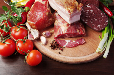 Meat products, bacon and sausages surrounded by vegetables and greens on a cutting board.
