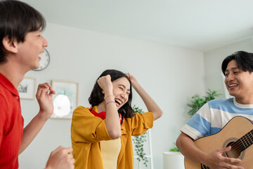 Diverse Asian friends playing guitar and dancing in living room at home. 