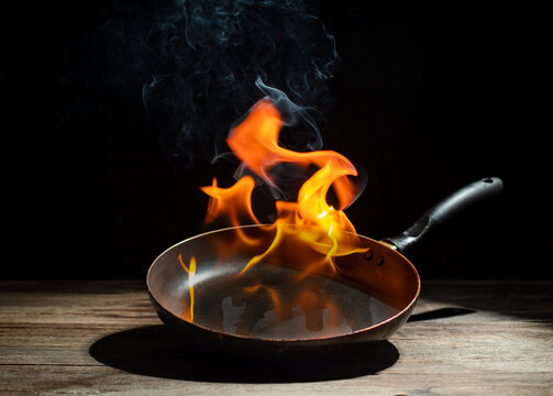 Black cooking pan with flames placed in kitchen on dark background table.