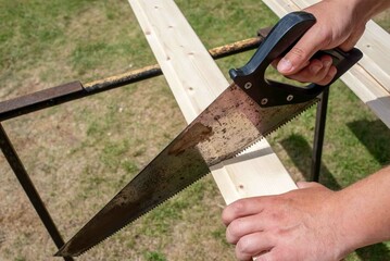 A saw in a man's hand saws a board.