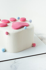 Birthday cake in the shape of trendy squish squishy paw on the white marble background. Pink Taba paw shaped cake for a child with white cream cheese frosting