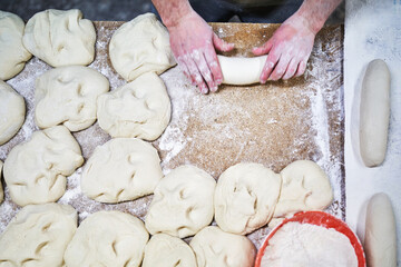 Top view of baker shaping bread dough on floured surface