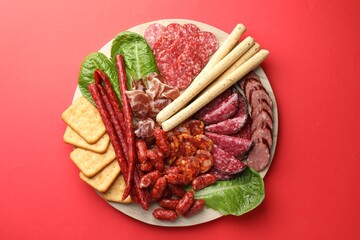 Different smoked sausages and other snacks on red background, top view