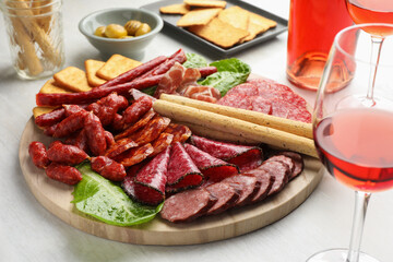 Different smoked sausages and other snacks served with wine on white table, closeup