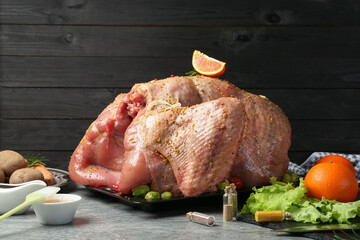 Whole raw turkey with ingredients for marinade and other products on grey table