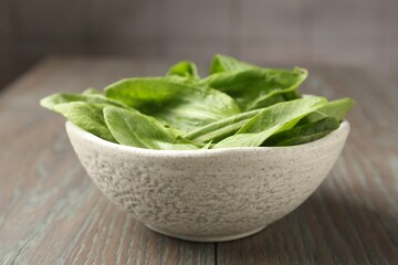 Fresh green sorrel leaves in bowl on wooden table, closeup