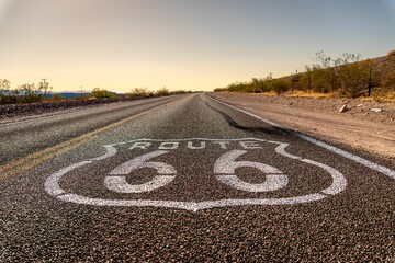 Iconic Route 66 road sign on an empty highway in a desert landscape.