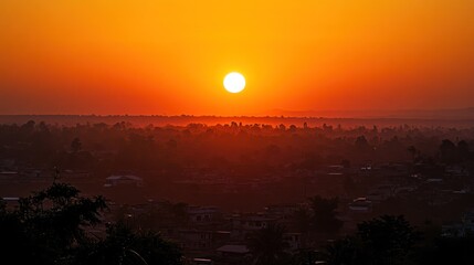 Vibrant sunrise over a hazy cityscape, casting a warm orange glow on the landscape.
