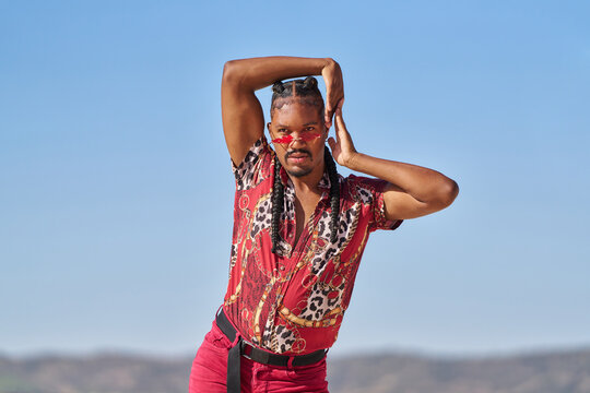 Young androgynous man dancing outdoors with red shirt and sunglasses