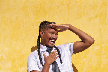 Stylish androgynous man shielding eyes from sun while laughing