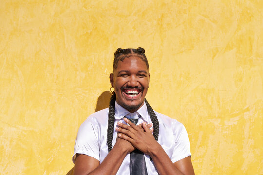 Young androgynous man smiling with hands on chest against yellow wall - Powered by Adobe