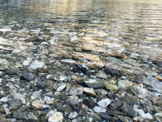 close-up of pebbles and stones under transparent mountain river water with soft ripples. natural clean water texture with light