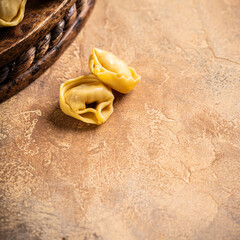 Healthy Italian food background with copy space. Freshly made tortellini Cappelletti pasta with prosciutto, elegantly arranged on a rustic wooden board