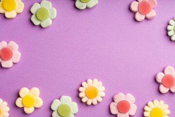 An arrangement of pastel-colored flower-shaped gummy candies with jelly centers on a purple background, creating a playful and sweet composition. Copy space for text