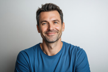 Fototapeta premium Friendly man smiling in casual blue t-shirt against light background