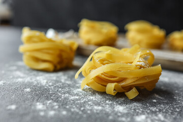 Raw nests of fettuccine pasta arranged on a light surface with a dark textured background....