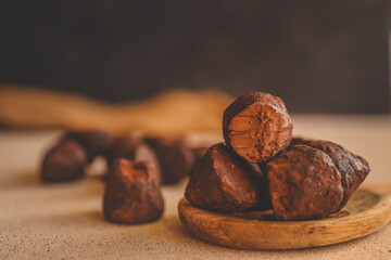 Stack of chocolate truffles on a wooden plate, one with a bite taken out, showing smooth filling and rich texture, with warm background lighting