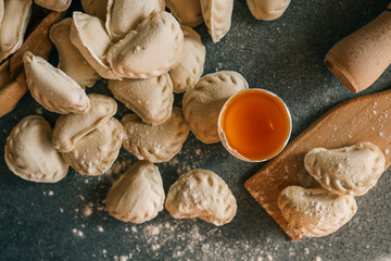 Top view of raw homemade dumplings on a floured kitchen surface with a wooden board, egg yolk, and rolling pin