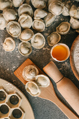 Homemade raw dumplings on a wooden spatula and floured table, surrounded by egg yolk, rolling pin, flour bowl, and dough mold — ingredients for traditional cooking