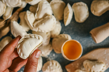 Close-up of a hand holding a raw frozen dumpling over a kitchen surface with flour, egg yolk, and other dumplings in the background