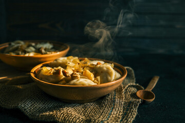 Traditional dumplings served in a rustic clay bowl with fried onions and steam rising, placed on...