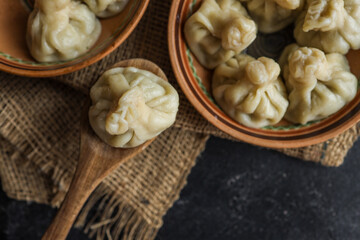 Close-up of a traditional Georgian khinkali dumpling served on a wooden spoon, placed beside two rustic ceramic bowls filled with more dumplings