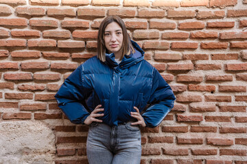 Young woman posing with hands on hips in front of brick wall