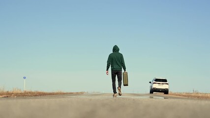 A man with a can of gasoline in his hand walks along the road to his car - Powered by Adobe