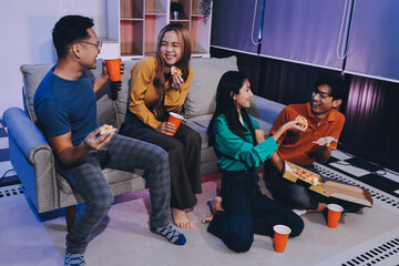 Fototapeta premium Happy young friends group having lunch at home. Asia family party eating pizza food and laughing enjoying meal while sitting at dining table together at house. Celebration holiday and togetherness.