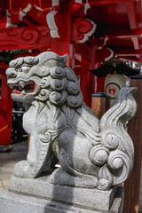 Obraz premium Detailed side view traditional Japanese komainu stone lion statue, guarding the vibrant red orange wooden structure of a buddhist temple's entrance. Stone figure has great cultural significance.