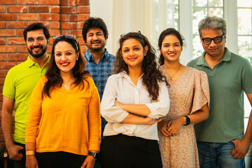 Confident Indian Asian business team in casuals, smiling, posing for photo in modern workspace