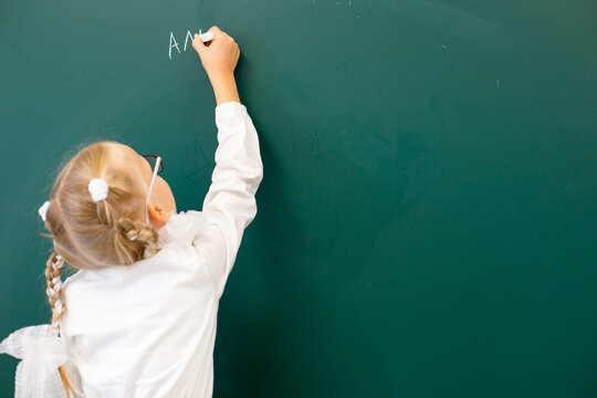 Knowledge for all A cheerful young girl wearing a graduation cap and glasses stands in front of a green chalkboard, holding a piece of chalk. She smiles with missing teeth. Elementary school