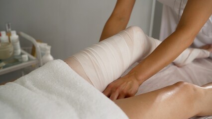 Massage therapist removing excess oil from a woman's legs using a towel after a massage session