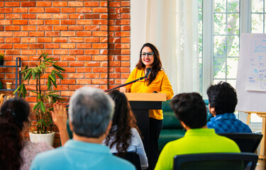 Indian Asian Confident life coach addressing entrepreneurs at a business event with a microphone