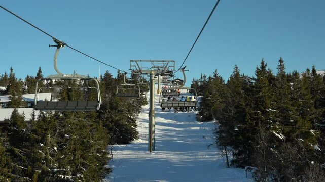 View from ski chairlift, in slow motion. People going up mountain in winter resort