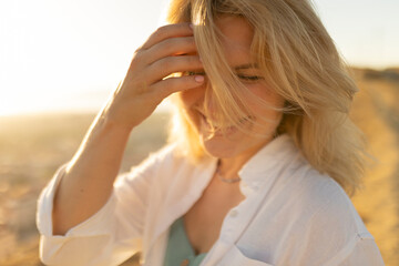 Blonde woman touching hair in golden sunlight at sunset