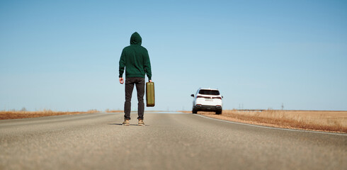 A man with a can of gasoline in his hand walks along the road to his car