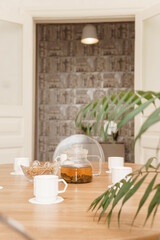 A peaceful arrangement featuring a glass teapot, cups, and a vase of white tulips on a wooden table, evoking warmth, simplicity, and serenity in the decor.